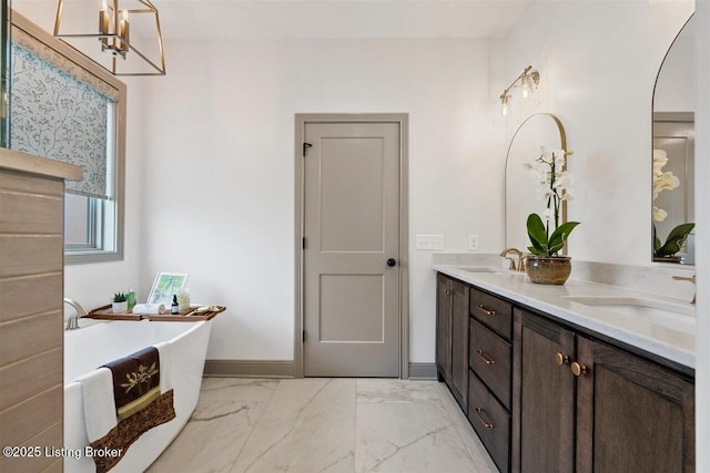 full bathroom with double vanity, a freestanding tub, a sink, and marble finish floor