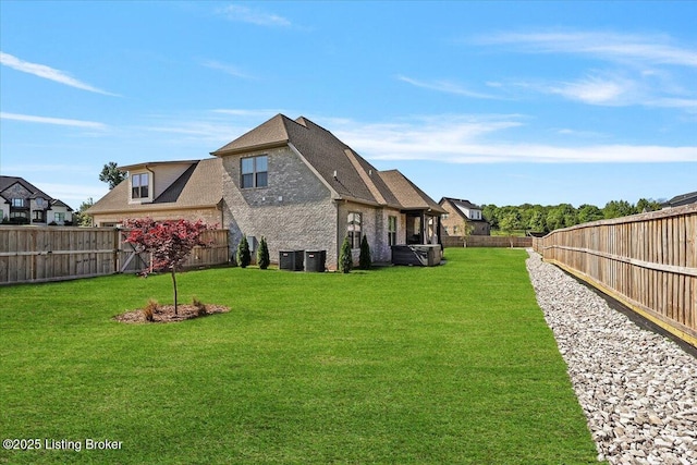 rear view of house featuring a yard, brick siding, a fenced backyard, and central air condition unit