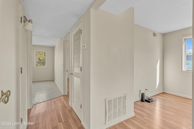 hallway with visible vents, light wood-style flooring, and a wealth of natural light