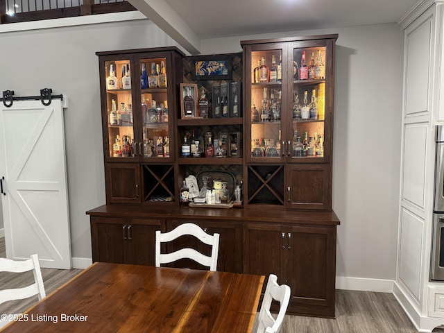 bar with baseboards, a barn door, wood finished floors, and stainless steel double oven