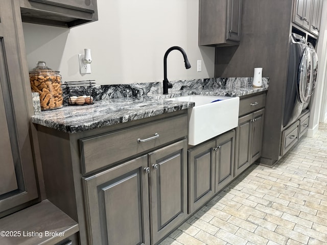 kitchen featuring dark stone counters, a sink, dark brown cabinets, and washer / dryer