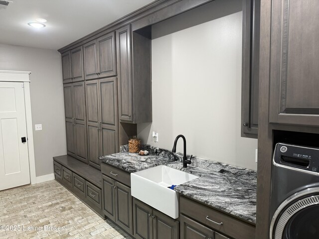 clothes washing area with a sink, baseboards, brick patterned floor, cabinet space, and washer / dryer