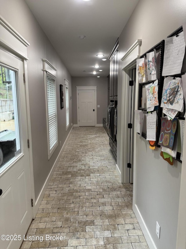 hallway with independent washer and dryer, brick floor, and baseboards