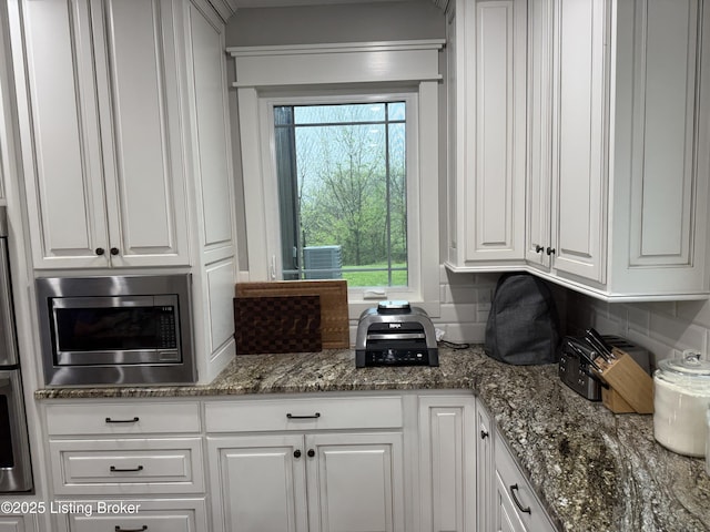 kitchen featuring stainless steel microwave, white cabinets, oven, stone counters, and backsplash