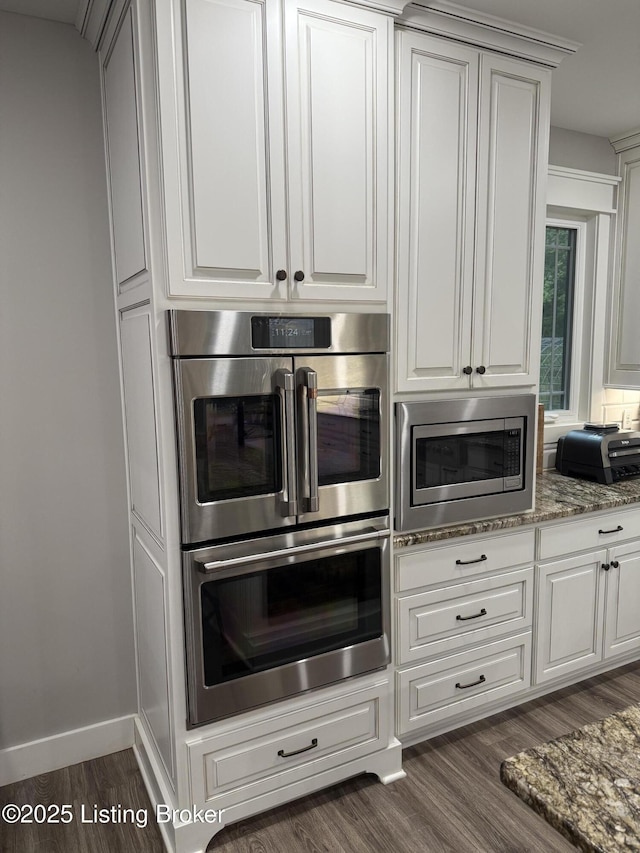 kitchen with appliances with stainless steel finishes, dark wood-type flooring, white cabinetry, and stone countertops