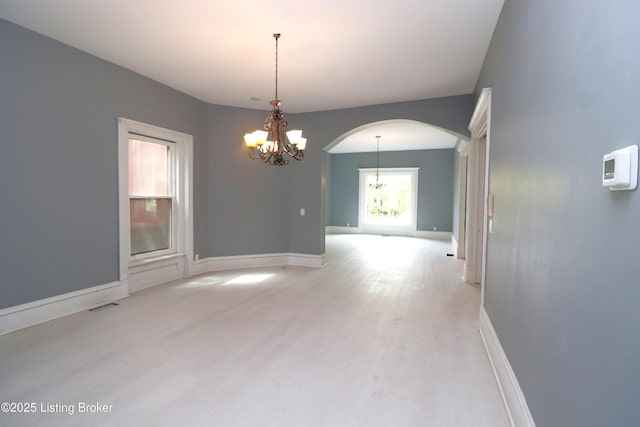 unfurnished room with arched walkways, light wood-style floors, baseboards, visible vents, and a notable chandelier