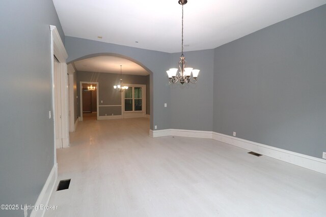empty room featuring visible vents, arched walkways, a notable chandelier, and light wood-style flooring
