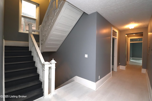 stairs with a textured ceiling, wood finished floors, and baseboards