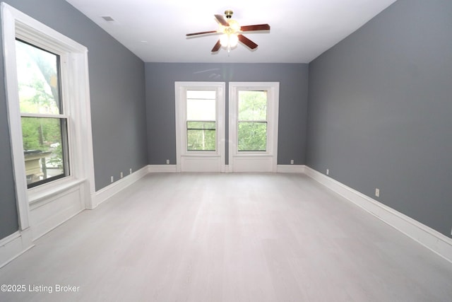 spare room with baseboards, visible vents, a ceiling fan, and light wood finished floors