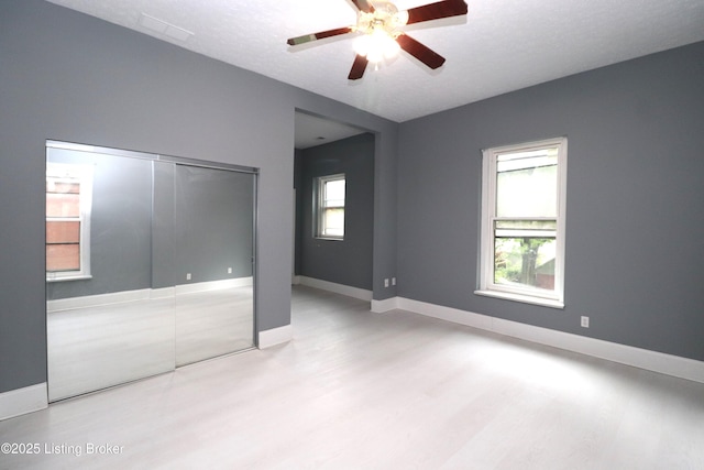 unfurnished bedroom with baseboards, wood finished floors, multiple windows, and a closet