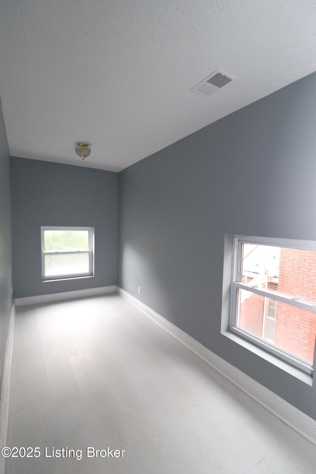 empty room featuring baseboards, visible vents, a healthy amount of sunlight, and a textured ceiling