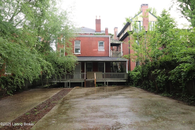 rear view of property featuring covered porch, a balcony, and a chimney
