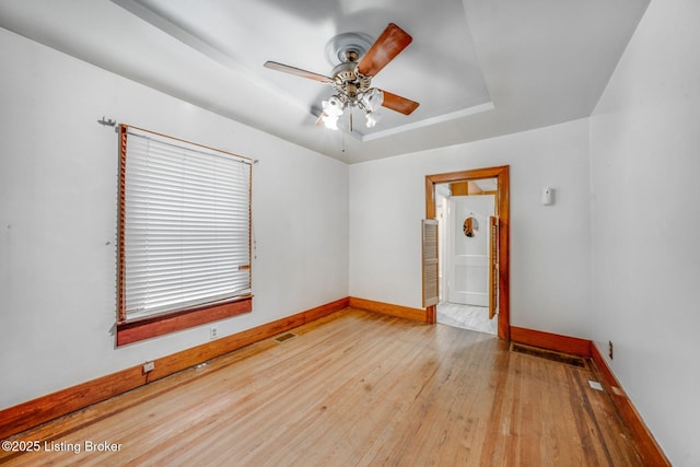 unfurnished room with wood finished floors, baseboards, visible vents, a ceiling fan, and a tray ceiling