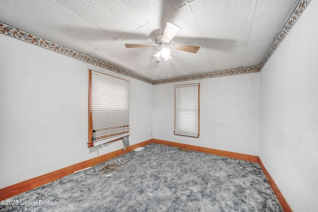 unfurnished room with a paneled ceiling, a ceiling fan, carpet flooring, and baseboards