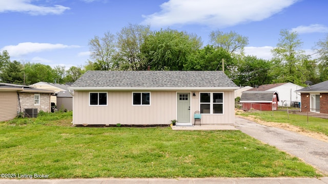 view of front of home featuring central air condition unit, roof with shingles, an outbuilding, and a front yard