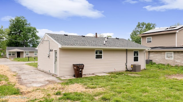 rear view of house with a lawn, central AC unit, and roof with shingles