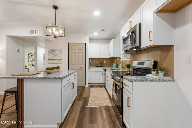 kitchen featuring visible vents, a center island, a sink, stainless steel appliances, and dark wood-type flooring