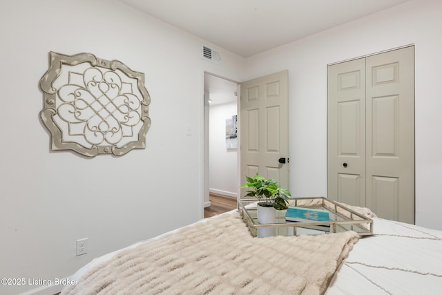 bedroom featuring visible vents, baseboards, wood finished floors, and a closet