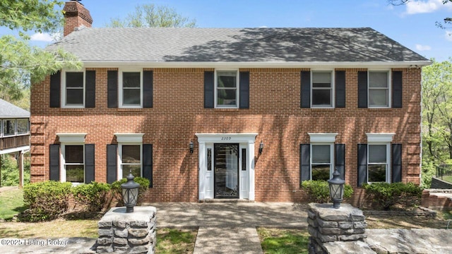 colonial inspired home with a chimney, brick siding, and a shingled roof