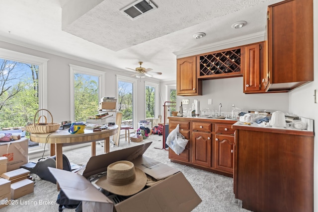 kitchen with brown cabinetry, a ceiling fan, visible vents, light carpet, and light countertops