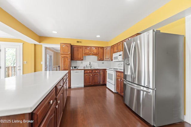 kitchen featuring white appliances, brown cabinetry, light countertops, a sink, and dark wood-type flooring