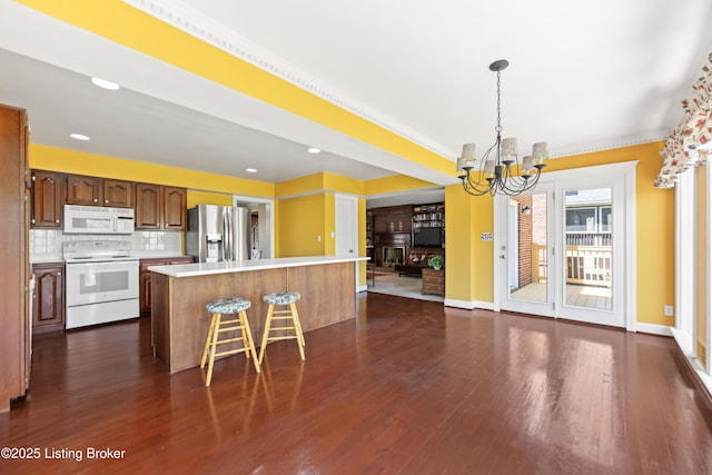 kitchen featuring dark wood-style flooring, a chandelier, white appliances, a center island, and light countertops