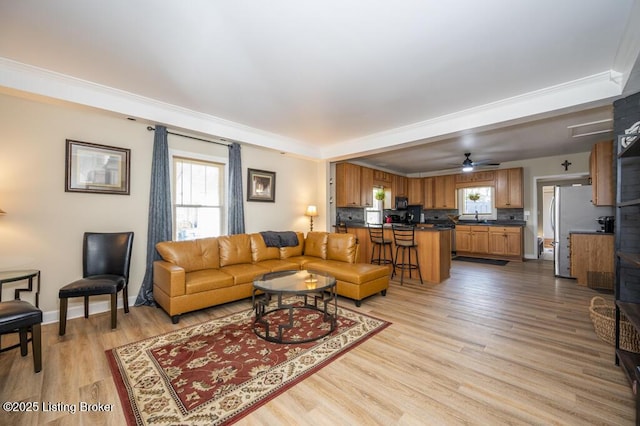 living area with ceiling fan, baseboards, light wood-style floors, and a tray ceiling
