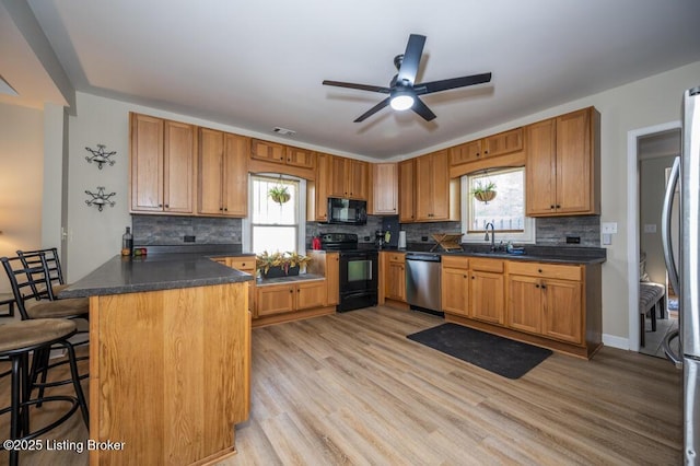 kitchen featuring decorative backsplash, black appliances, ceiling fan, dark countertops, and a sink
