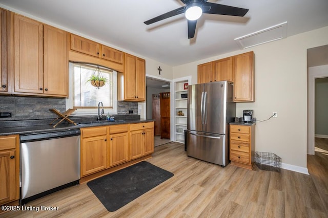 kitchen with a sink, a ceiling fan, backsplash, dark countertops, and appliances with stainless steel finishes