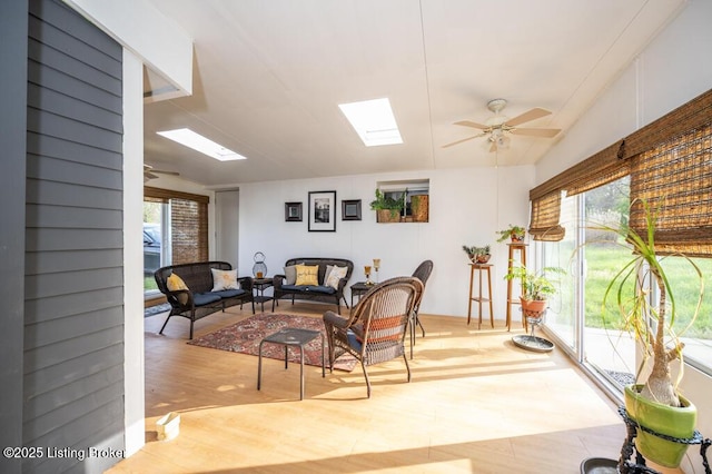 living room with a wealth of natural light, a skylight, ceiling fan, and wood finished floors