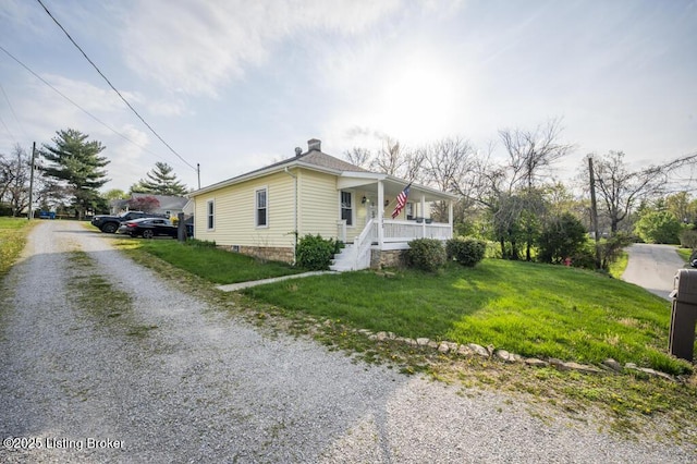 view of property exterior with a chimney, a porch, gravel driveway, and a lawn