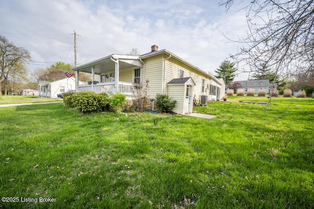 view of side of home featuring central air condition unit, a chimney, a yard, and a porch