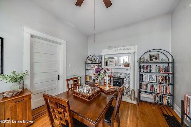 dining space with ceiling fan, a fireplace, and wood finished floors