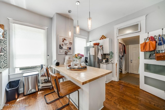 kitchen featuring stainless steel fridge, butcher block countertops, dark wood-type flooring, and a kitchen breakfast bar