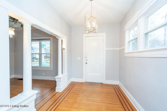 entryway featuring light wood-style floors, baseboards, an inviting chandelier, and ornate columns