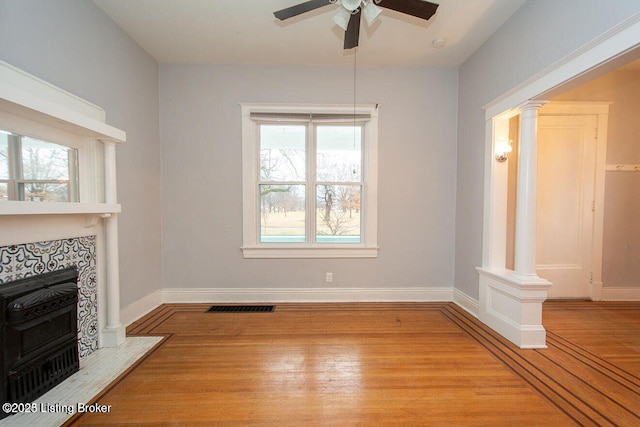 unfurnished living room with visible vents, decorative columns, wood finished floors, a tile fireplace, and a ceiling fan