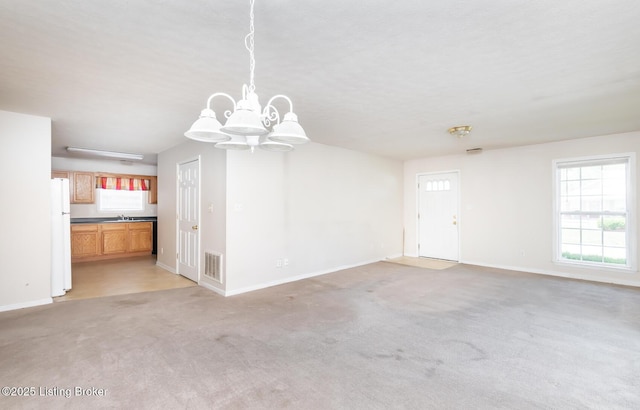 unfurnished living room featuring visible vents, baseboards, a notable chandelier, and light colored carpet