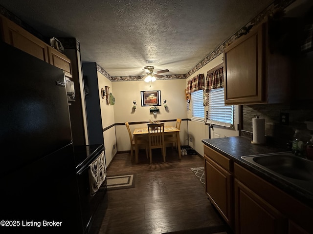 kitchen with dark countertops, a textured ceiling, dark wood finished floors, freestanding refrigerator, and a ceiling fan