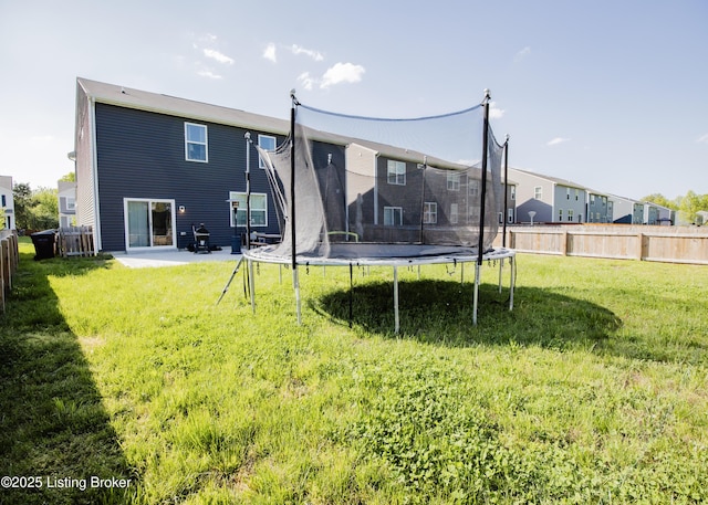 rear view of house featuring a lawn, a trampoline, a fenced backyard, and a patio area