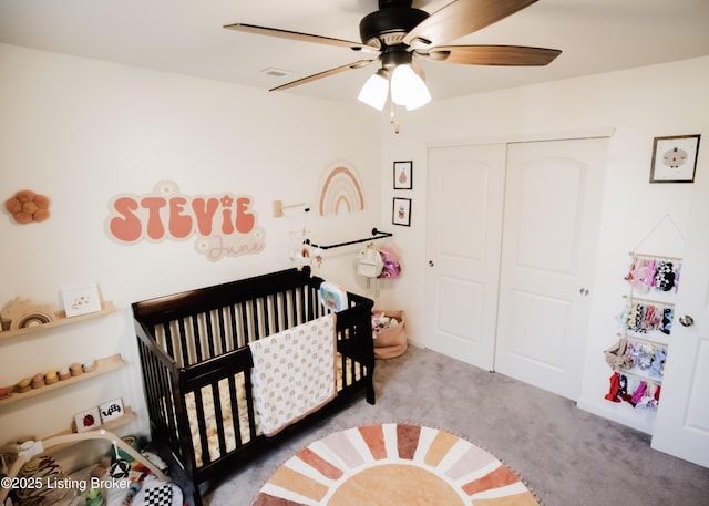 carpeted bedroom with a crib, a ceiling fan, and a closet