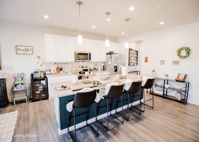 kitchen featuring stainless steel microwave, stove, light wood-type flooring, white refrigerator with ice dispenser, and an island with sink