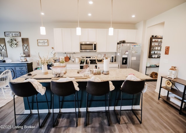 kitchen featuring wood finished floors, appliances with stainless steel finishes, a large island with sink, white cabinetry, and a kitchen breakfast bar