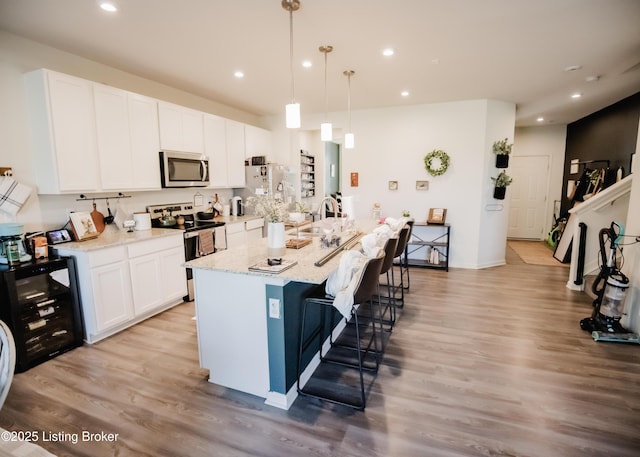 kitchen with appliances with stainless steel finishes, a kitchen island with sink, light wood-style flooring, and white cabinets