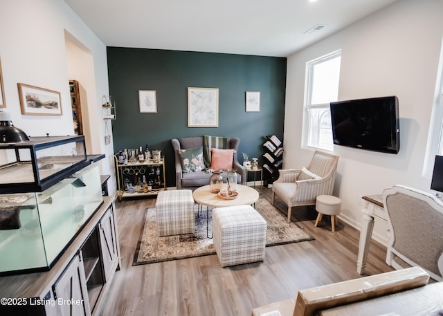 living room with an accent wall, wood finished floors, visible vents, and baseboards