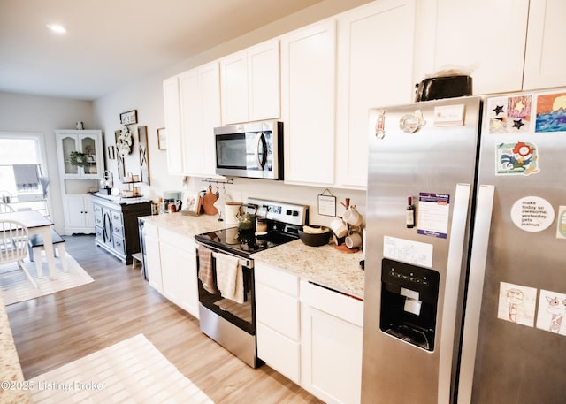 kitchen featuring appliances with stainless steel finishes, light stone counters, light wood-style flooring, and white cabinets