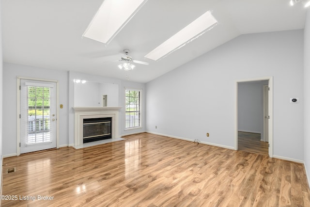 unfurnished living room with visible vents, a fireplace with flush hearth, baseboards, lofted ceiling with skylight, and light wood-style floors