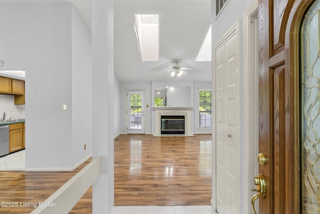 unfurnished living room with ceiling fan, a skylight, a sink, light wood finished floors, and a glass covered fireplace