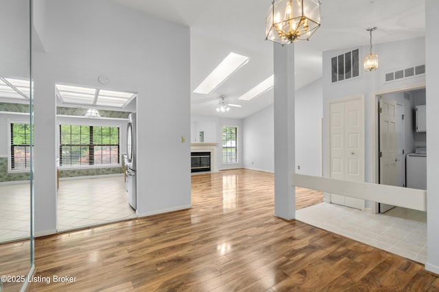 unfurnished living room with visible vents, washer / clothes dryer, wood finished floors, and high vaulted ceiling