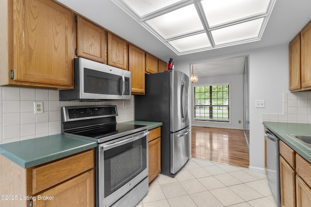 kitchen with brown cabinets, stainless steel appliances, baseboards, light tile patterned floors, and backsplash