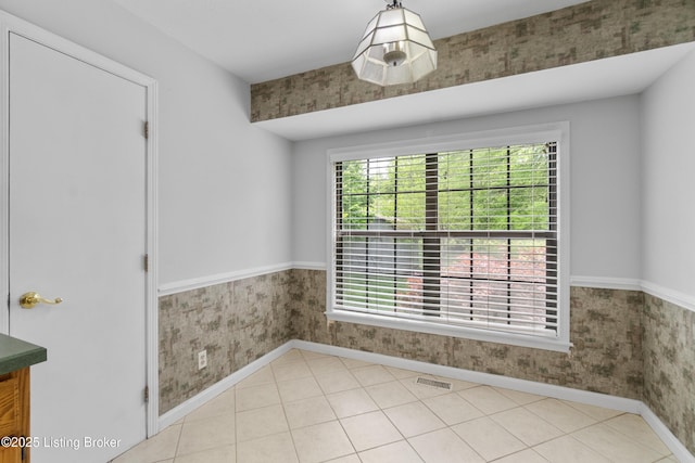 unfurnished dining area with visible vents, baseboards, a wainscoted wall, and wallpapered walls